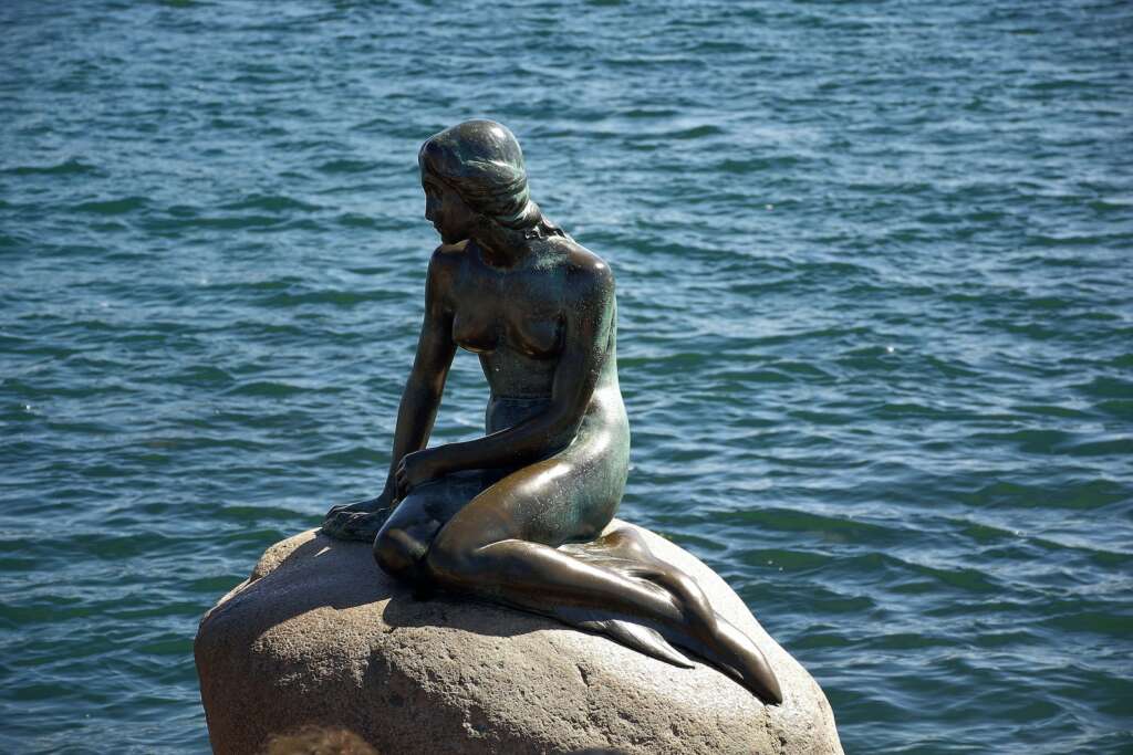 A statue of a mermaid sitting on a rock and looking towards the sea