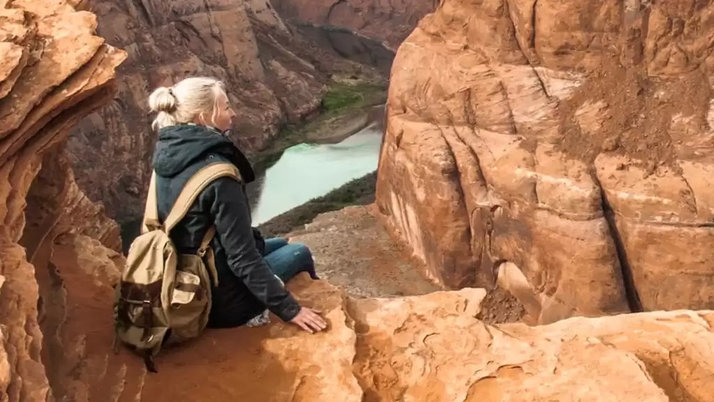 A majestic woman, gracefully perched atop a towering mountain peak, adorned with a backpack.