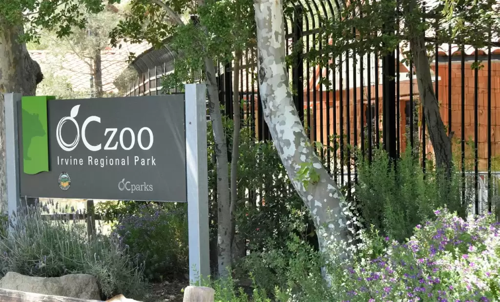 The board of Orange County Zoo is placed under the trees besides grass