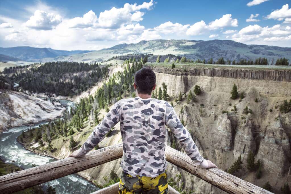 A man is standing on the edge of mountain for taking picture under the blue sky