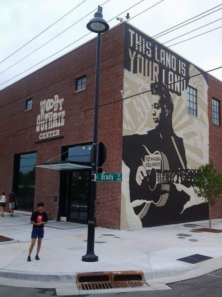 A man is standing in front of the best things to do in Tulsa Woody Guthrie Center under the blue sky