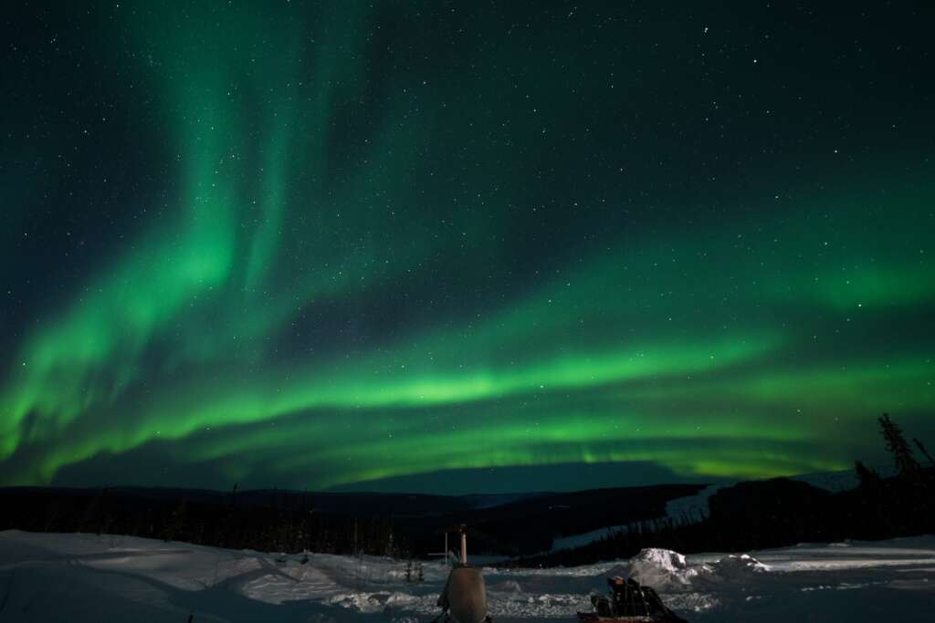visit a green and purple sky over a snowy landscape is one of the best time to visit the Alaska