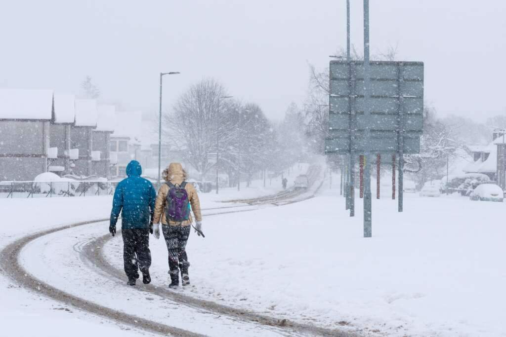 2 person walking on snow covered road during daytime in Scotland, it is the best time to visit Scotland