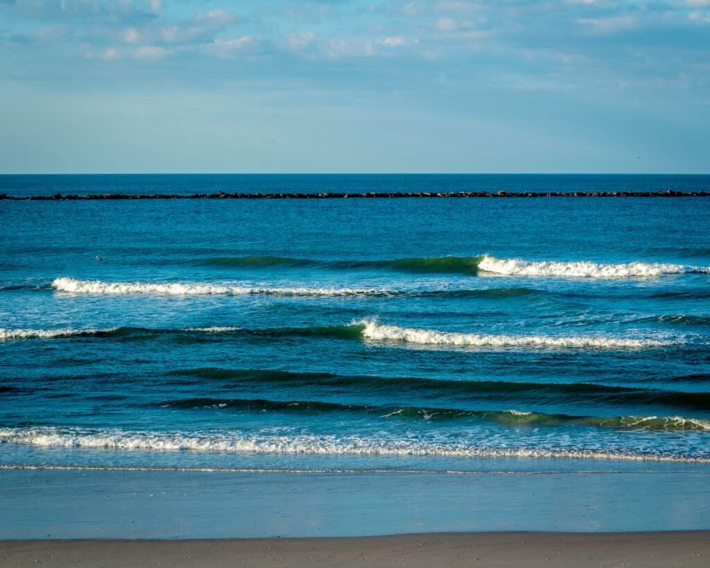 a body of water with waves coming in to shore under the blue sky, It is New Smyrna beach one of the shark-prone coastal destinations in the USA