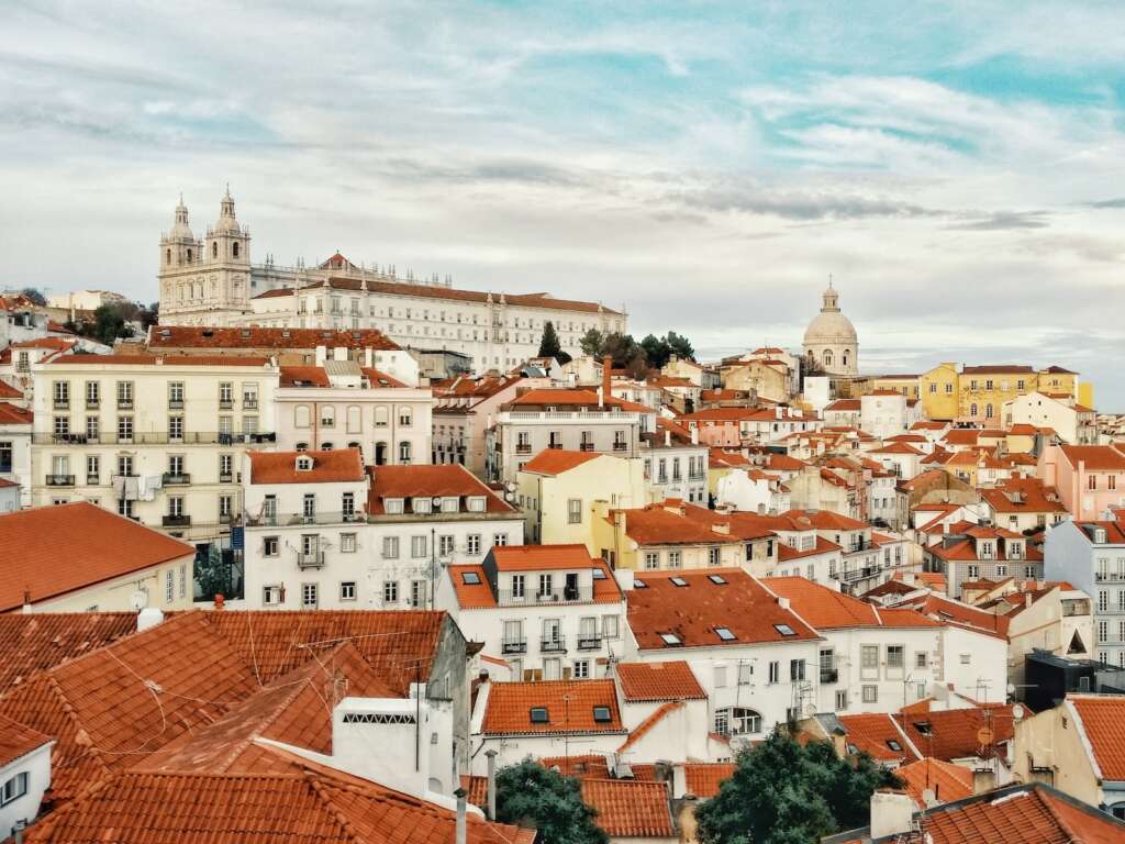 city landscape photography of white and red concerete buildings during daytime. if you are looking where to stay in Lisbon for sightseeing. Then must visit Alfama.