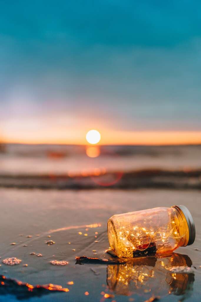 Summer: A clear glass mason jar on beach during sunset